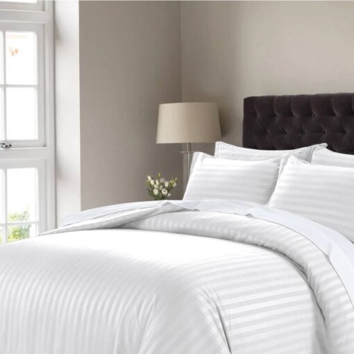 White striped comforter set with matching pillow shams on a bed with a dark tufted headboard in a modern bedroom setting.