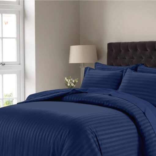 Dark blue striped comforter set with matching pillow shams on a bed with a dark tufted headboard in a modern bedroom setting.